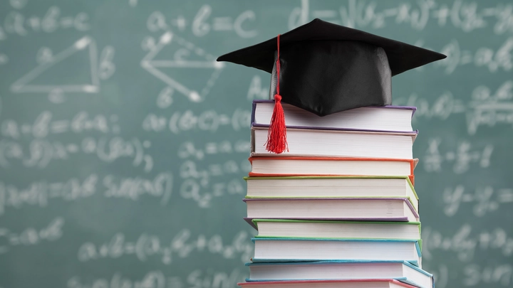 stack of books with grad cap on top and chalkboard behind