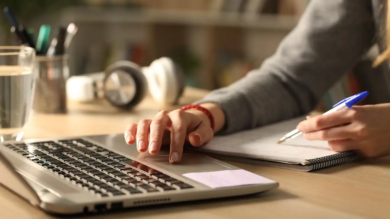 Person writing on a notepad whilst using a laptop