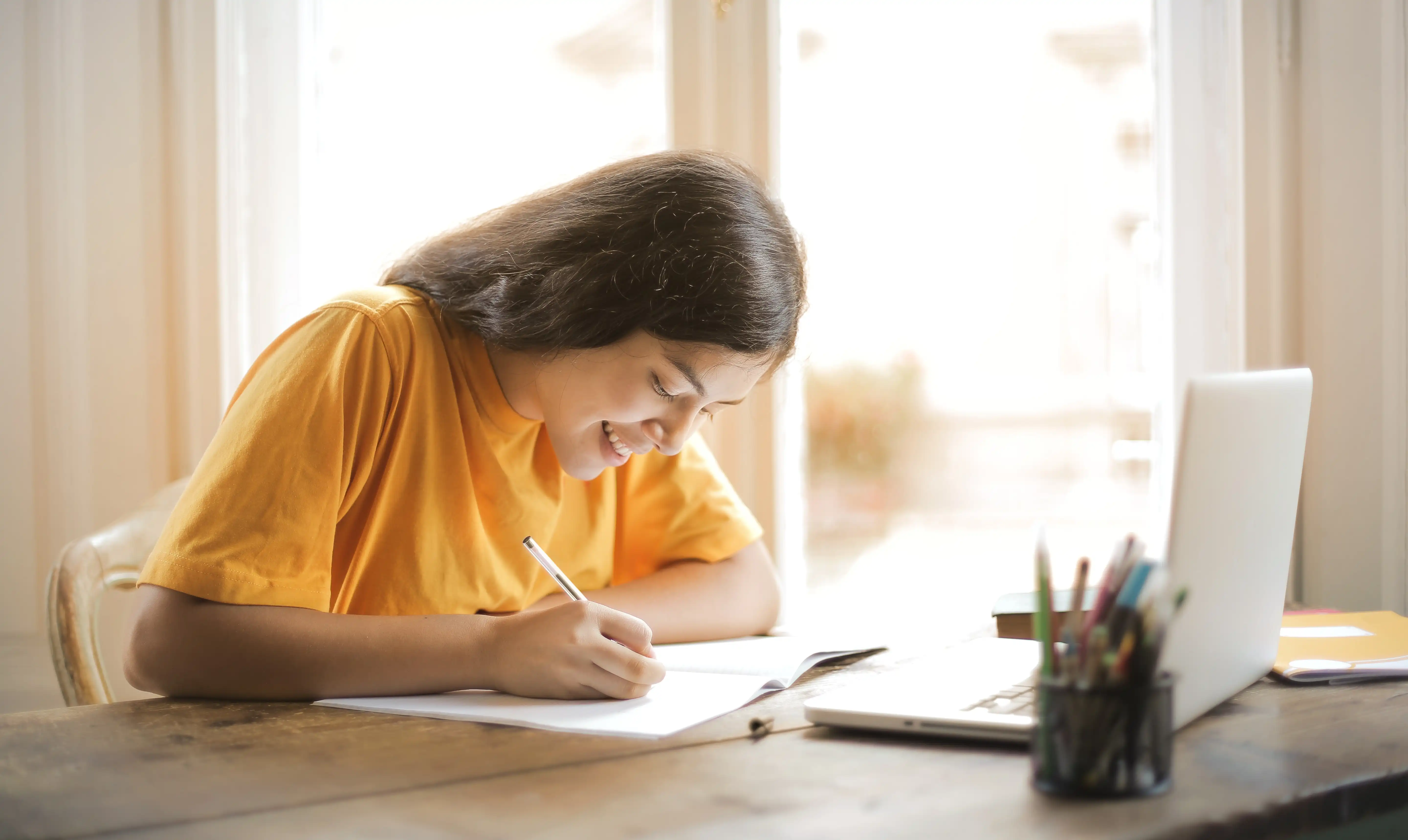 woman smiling writing something with laptop on table in front of her