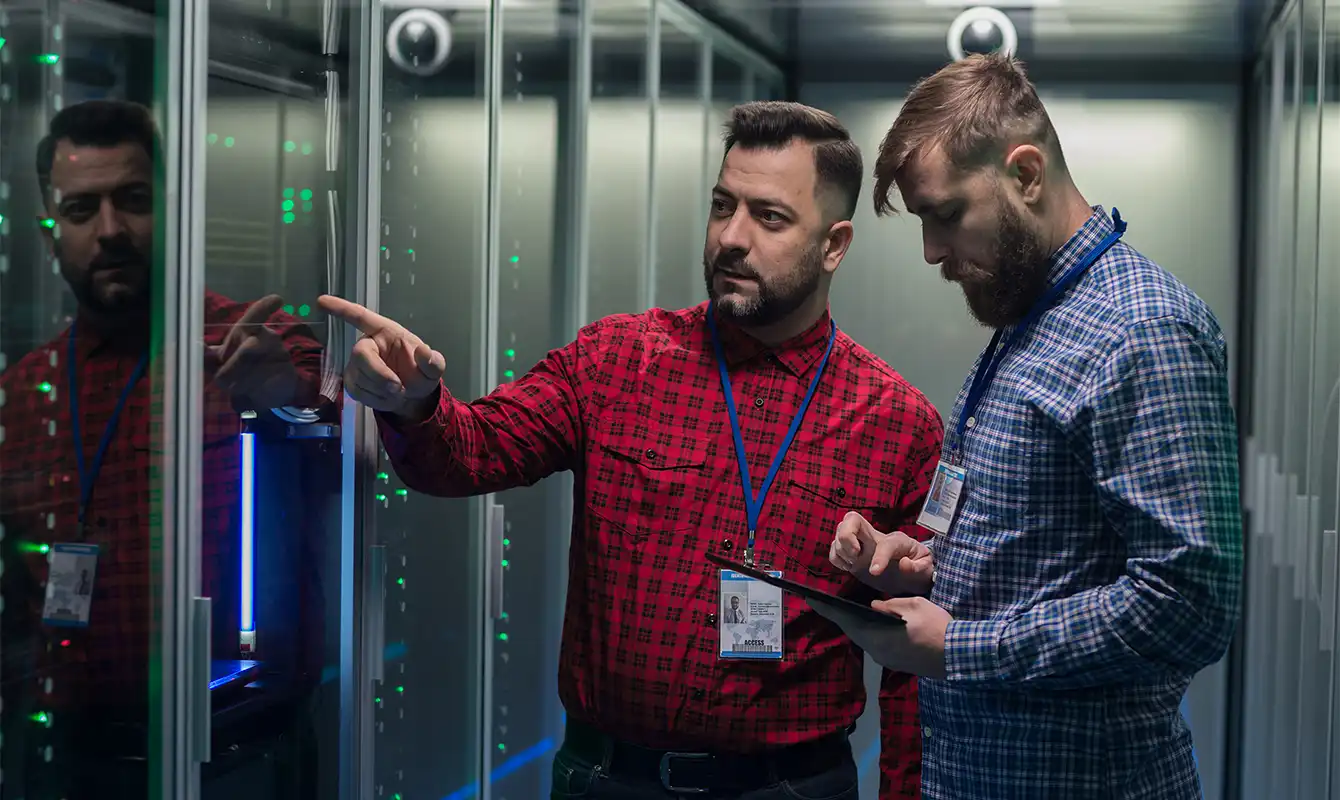 two men in server room, one pointing to server, one looking at ipad