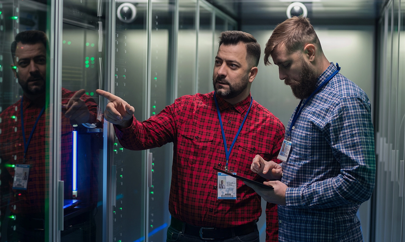 two men in server room, one pointing to server, one looking at ipad